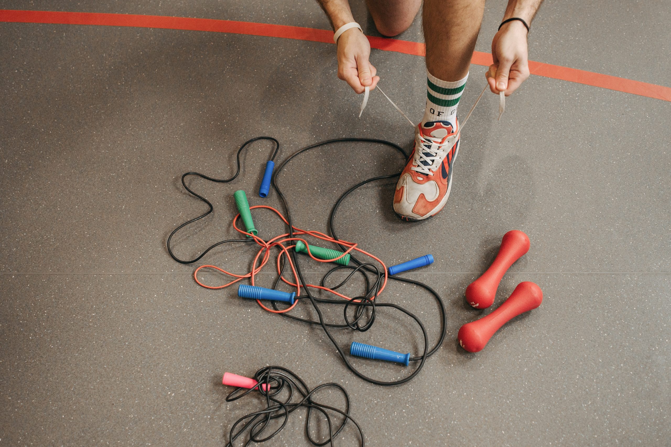 A Man Tying Shoe Lace Near Jump Ropes on the Floor